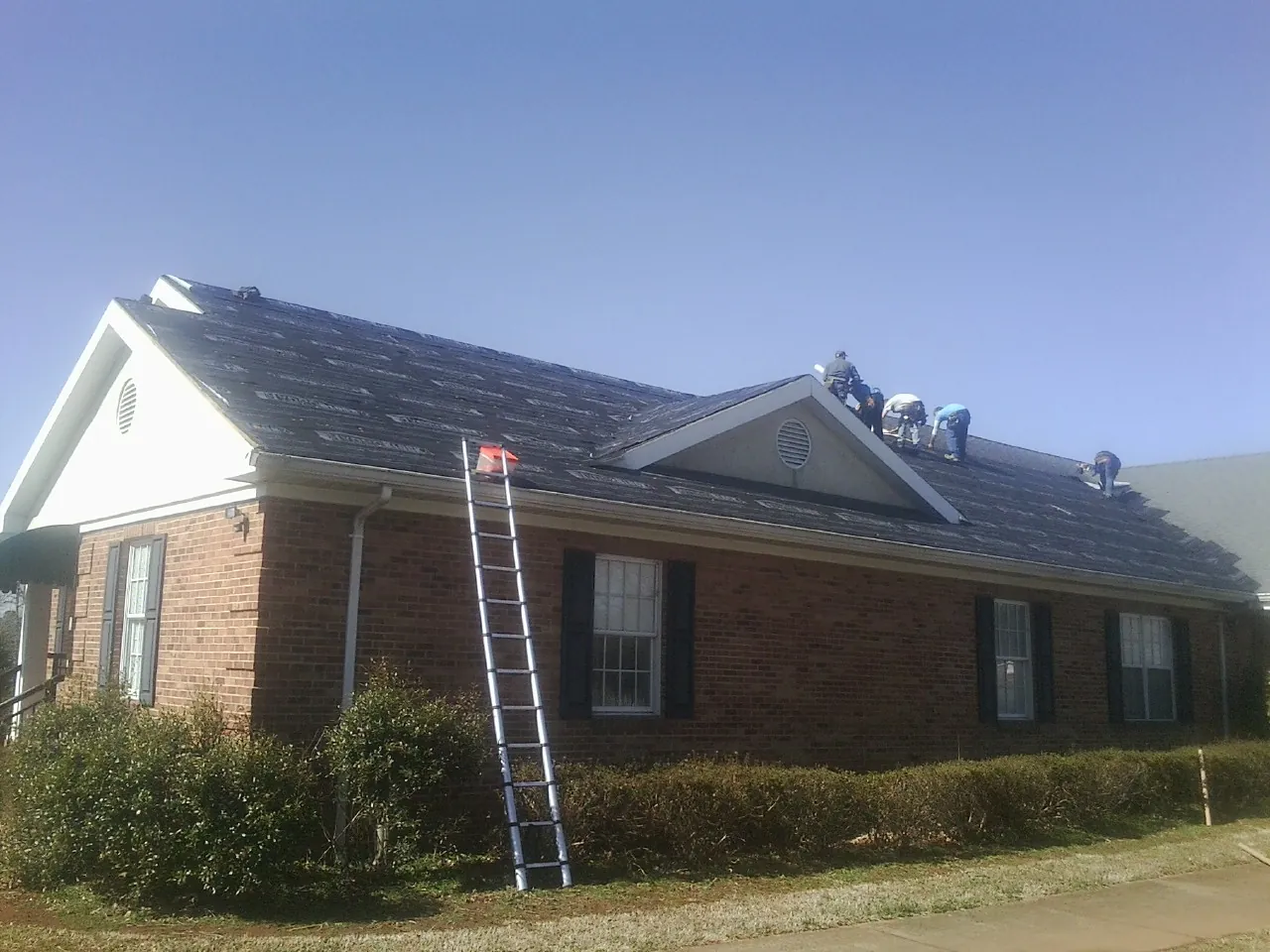 Crew tearing shingles off a brick ranch roof with a ladder set — Emergency Roof Repair work by our crew in Westtown