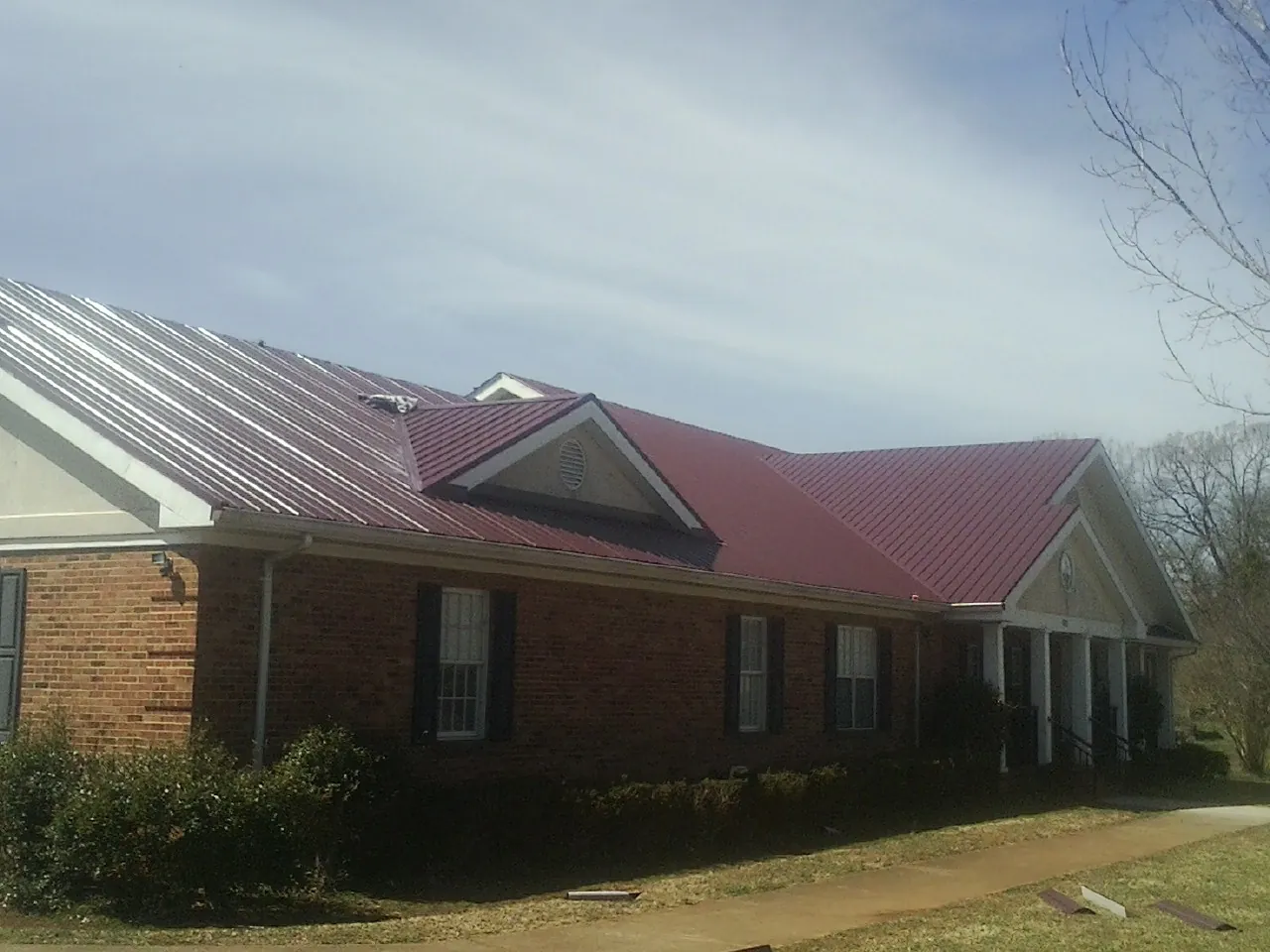 Red metal roof with gabled entries on a long brick building, from a Hail Damage Roof Repair job in Westtown