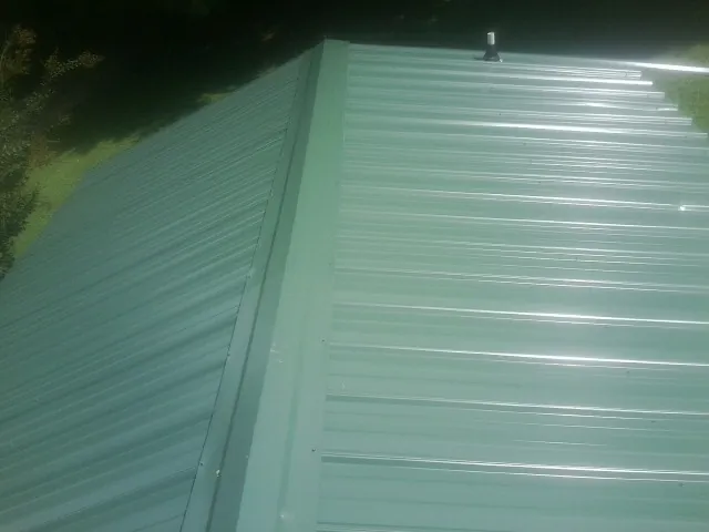 New green metal panels meeting at the ridge of a roof — Flat Roof Repair work by our crew in Westtown