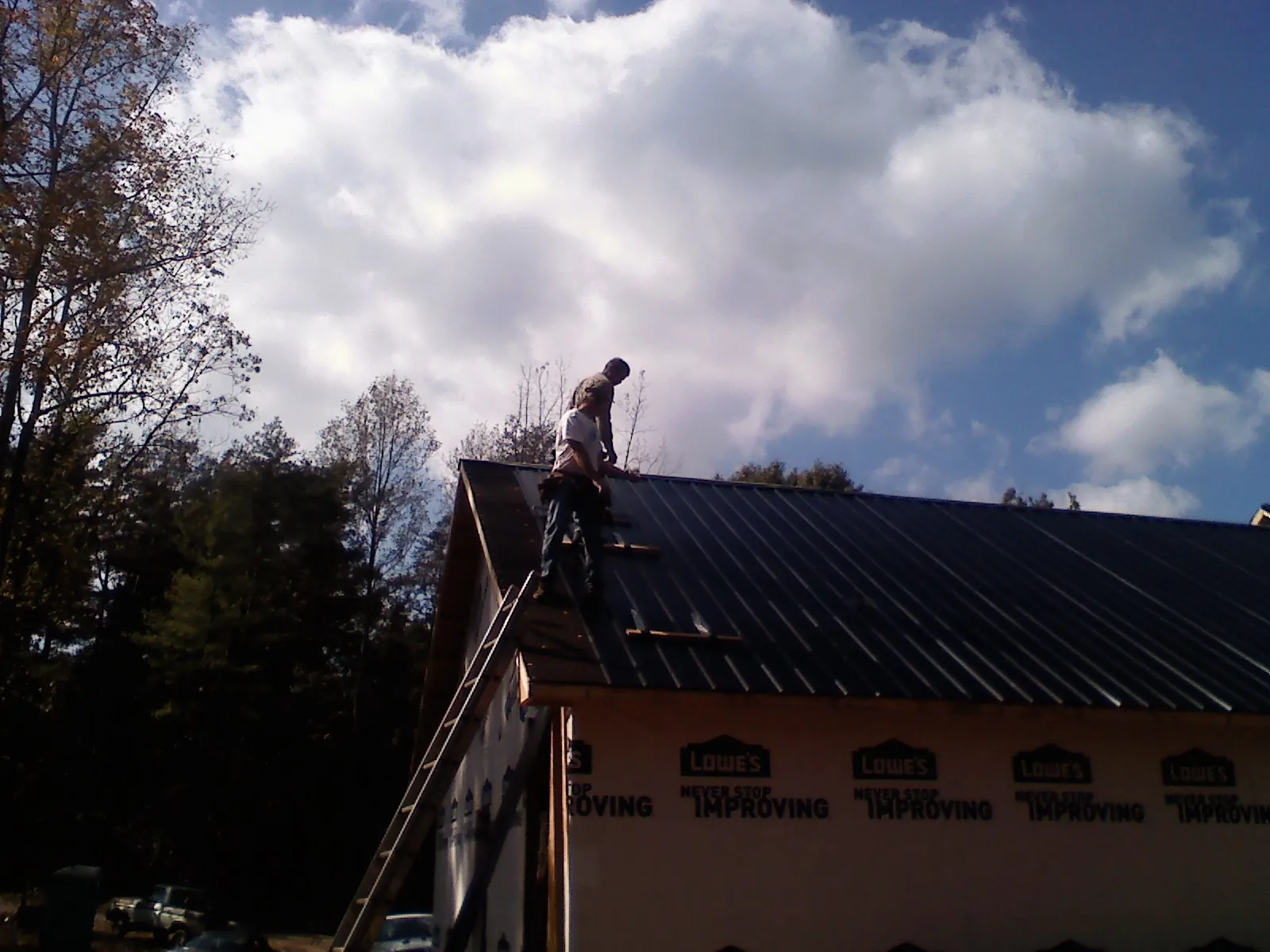Roofer fastening dark metal panels high against a cloudy sky, from a Roof Inspection job in Westtown