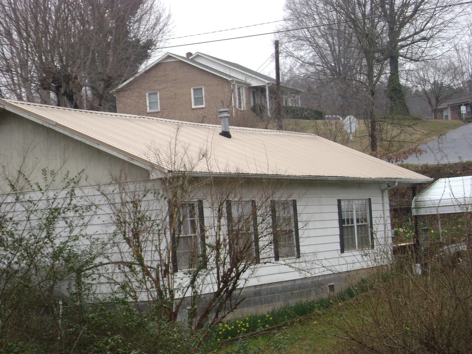 Tan metal roof on a white sided house set into a hillside — Commercial Roofing by Roofing Brothers in Westtown